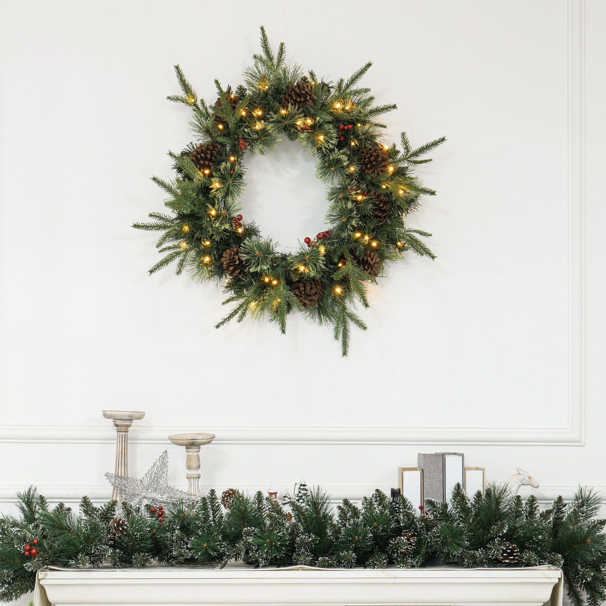 60-inch winter wreath with pinecones, berries & warm LED lights styled above a mantle — festive, lifelike branches in a rustic countryside setting.