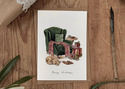 Illustrated Christmas card featuring a cosy green armchair, dog curled up on floor and wrapped gifts, — evokes countryside calm and seasonal warmth.