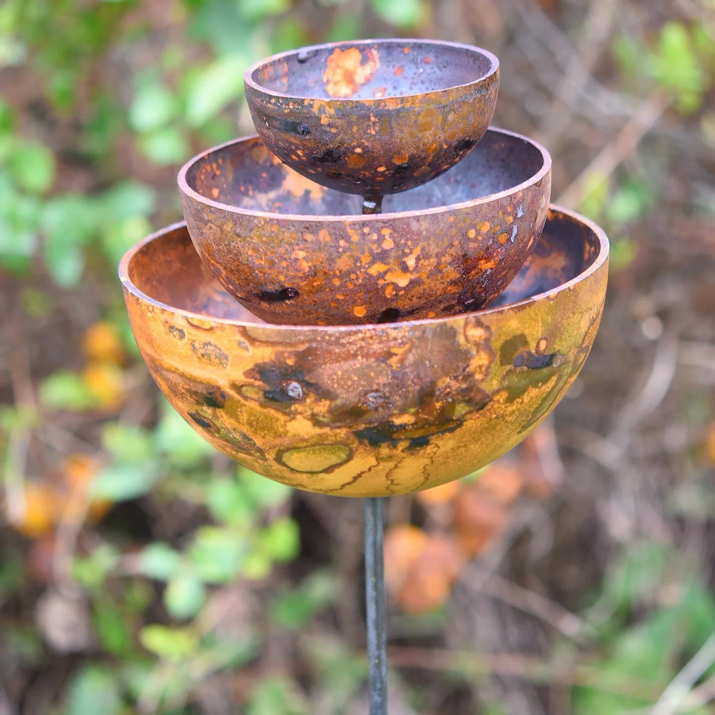 Three-tier rusted metal rain catcher fountain garden decor with blurred natural background
