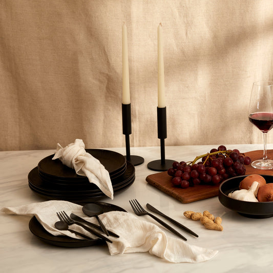 Alverley White cotton napkin set styled on a marble table with black cutlery, red wine, grapes, black candlesticks, and rustic bowls of onions, garlic, and peanuts for soulful countryside dining.