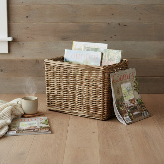 Antique wicker magazine rack with magazines on wooden floor, warm walls and hot coffee in a rustic countryside setting.