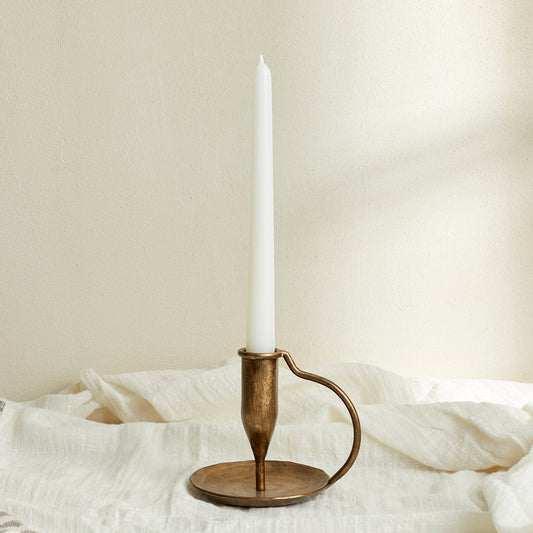 Ashbourne iron candle holder with taper candle, brushed gold tones glowing softly atop white linen—evokes rustic charm and timeless countryside ritual.