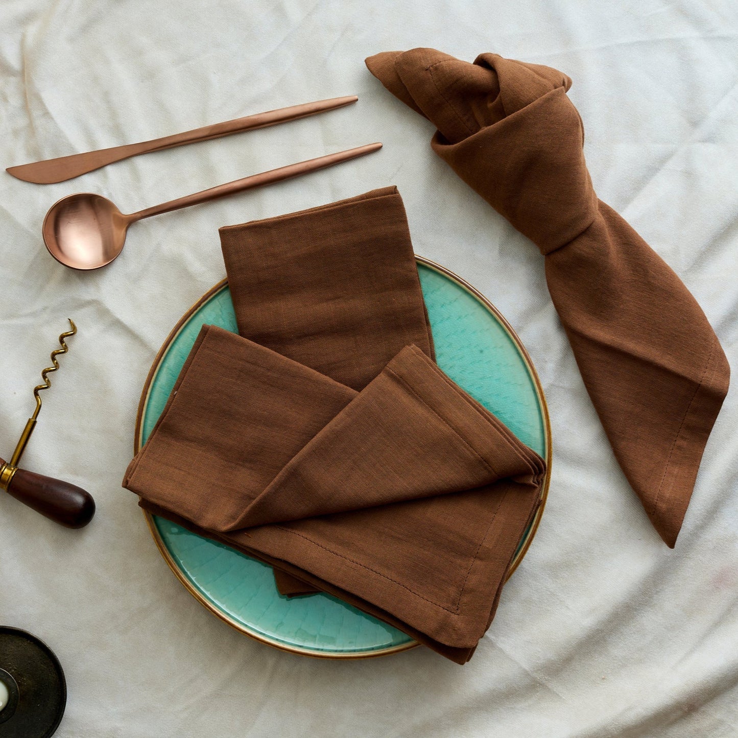 Branwell Brown muslin napkin set in soft cotton, styled with rose gold cutlery, corkscrew, and a knotted napkin laid on a jade pottery plate for rustic countryside dining.