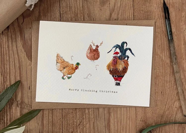 Merry Clucking Christmas greeting card featuring a cockerel and two chickens dressed in festive hats and shoes. Whimsical countryside-inspired design.