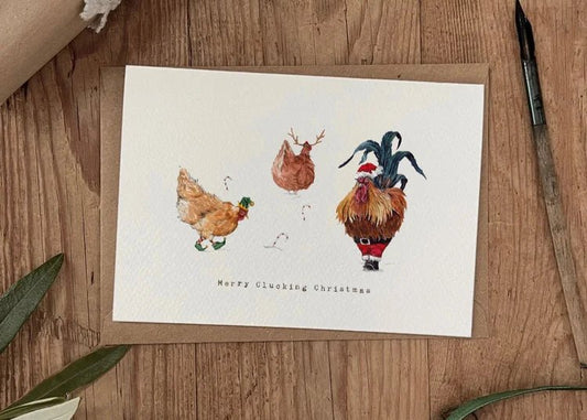 Merry Clucking Christmas greeting card featuring a cockerel and two chickens dressed in festive hats and shoes. Whimsical countryside-inspired design.