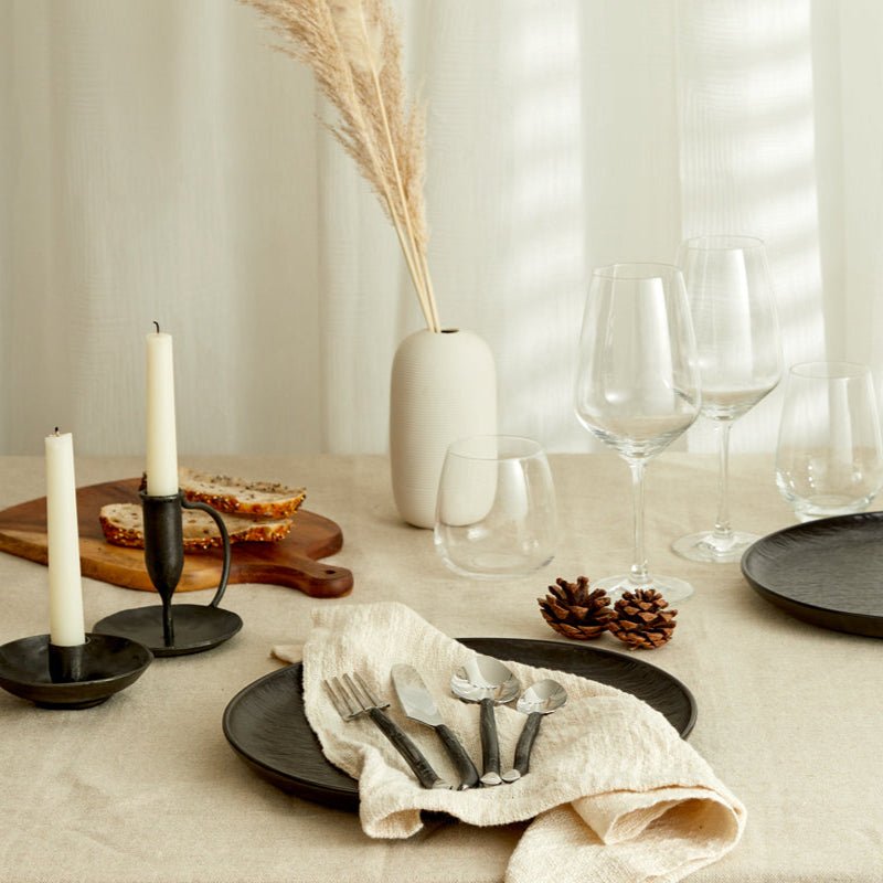 Elmswell silver cutlery set styled in a table setting with white linen, black plate, and folded napkin—evokes timeless hosting and rustic elegance.