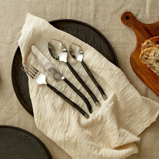 Elmswell silver cutlery set styled on white linen table with black plate and folded napkin—evokes timeless elegance and soulful countryside hosting.