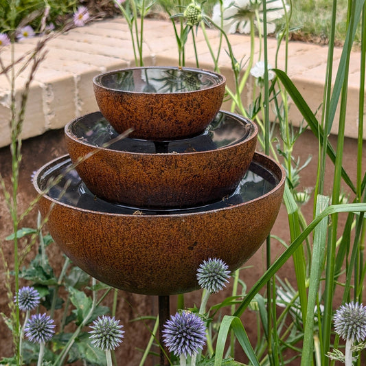 Rusty rain catcher fountain with layered metal bowls, warm orange patina, sculptural plant support and bird feeder for heritage-inspired garden styling.