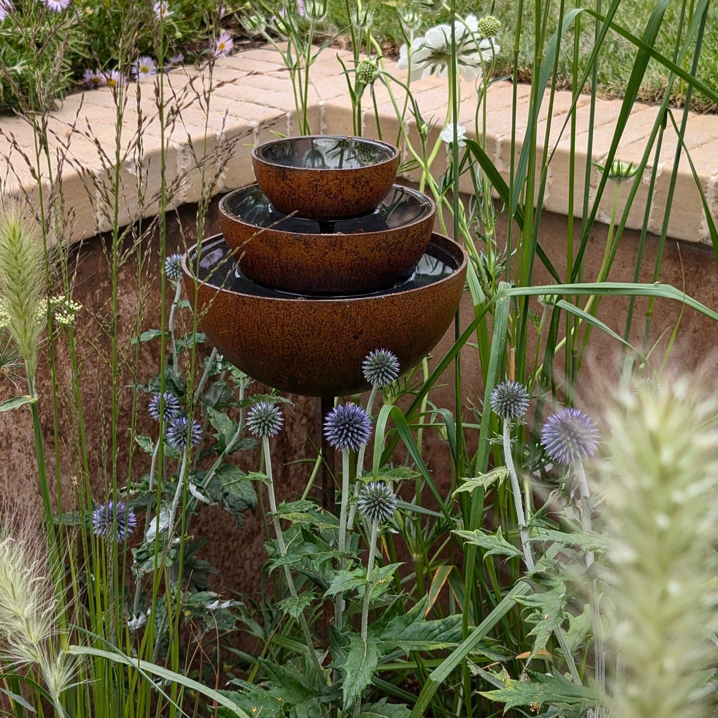 Rusty rain catcher fountain with layered metal bowls, sculptural plant support shown for clear heritage garden styling.
