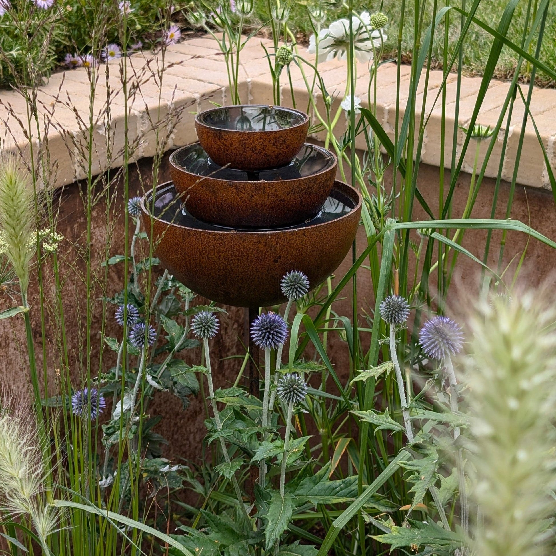 Rusty rain catcher fountain with layered metal bowls, sculptural plant support shown for clear heritage garden styling.