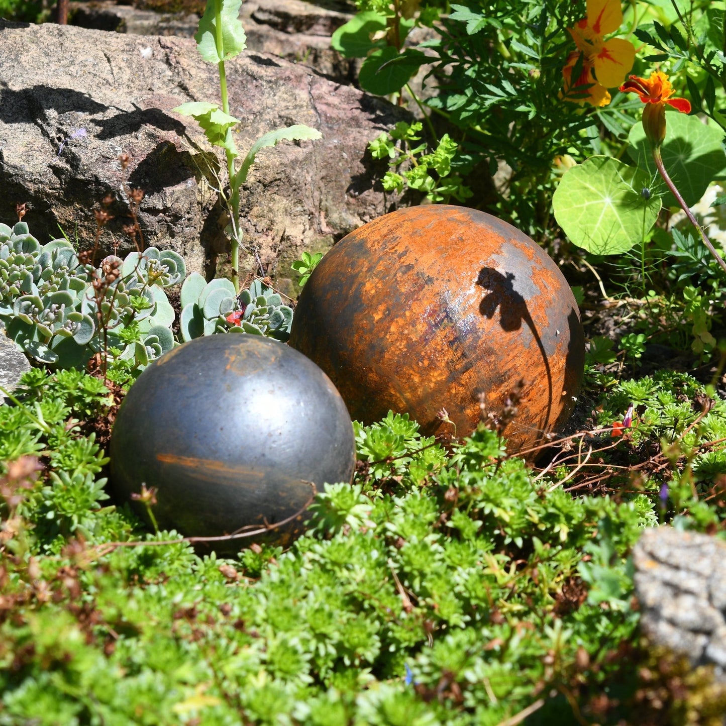 Rusted steel garden ball trio nestled in greenery, handcrafted outdoor sculptures from The Timeless Trading Co. for soulful countryside styling.
