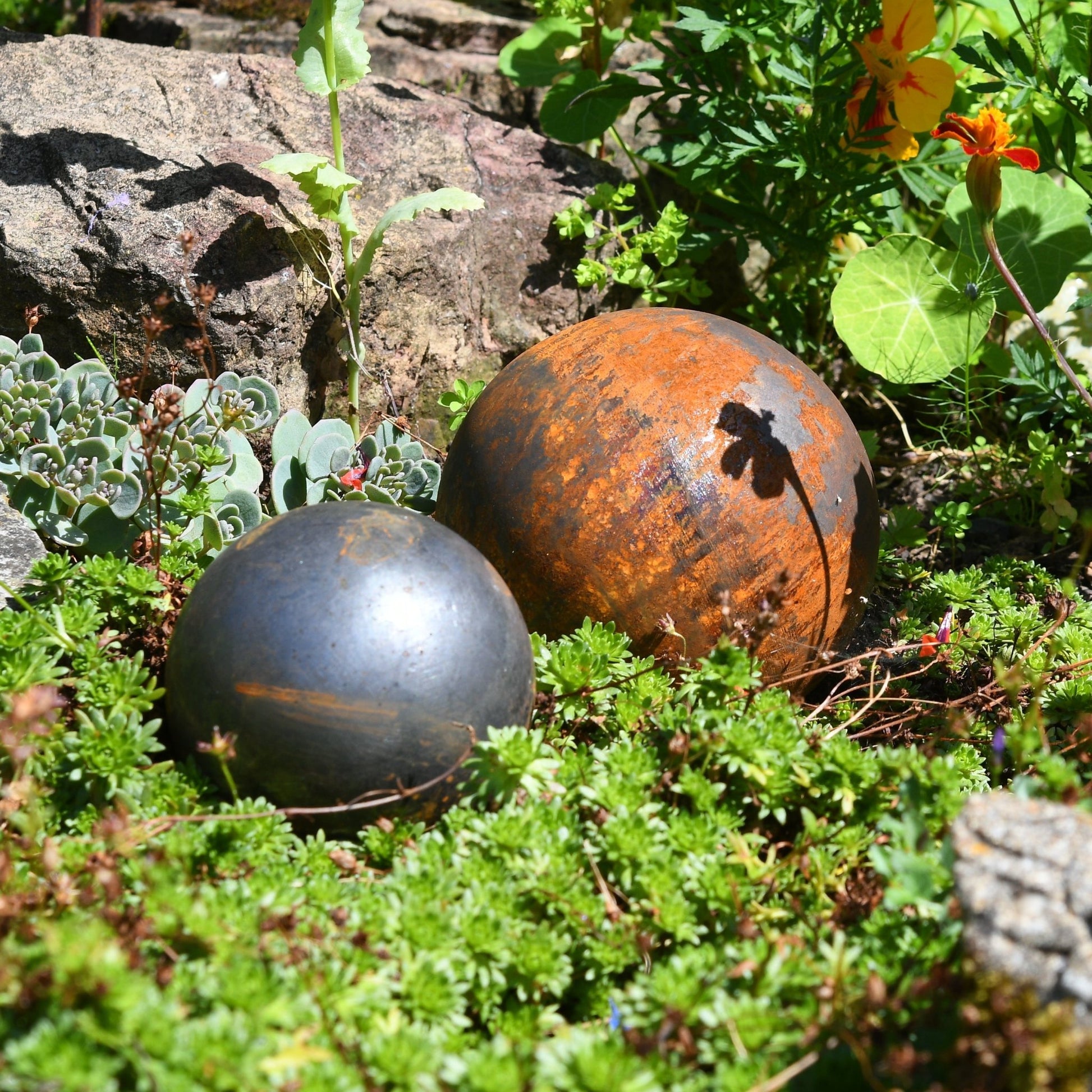 Rusted steel garden ball trio nestled in greenery, handcrafted outdoor sculptures from The Timeless Trading Co. for soulful countryside styling.
