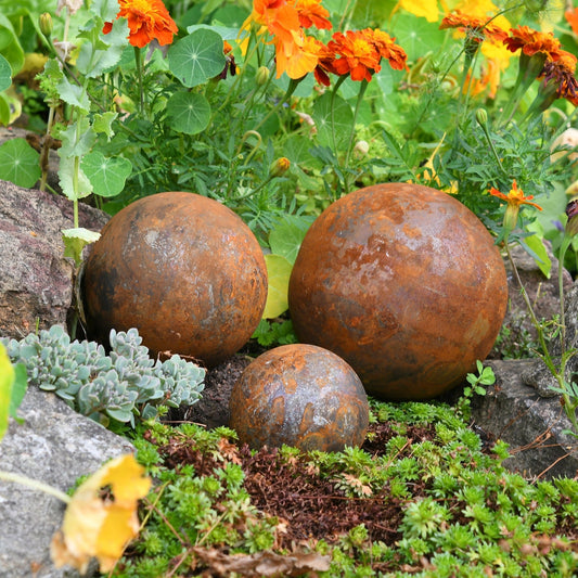 Rusted steel garden ball trio in small and large sizes, handcrafted outdoor sculptures with weathered patina from The Timeless Trading Co.