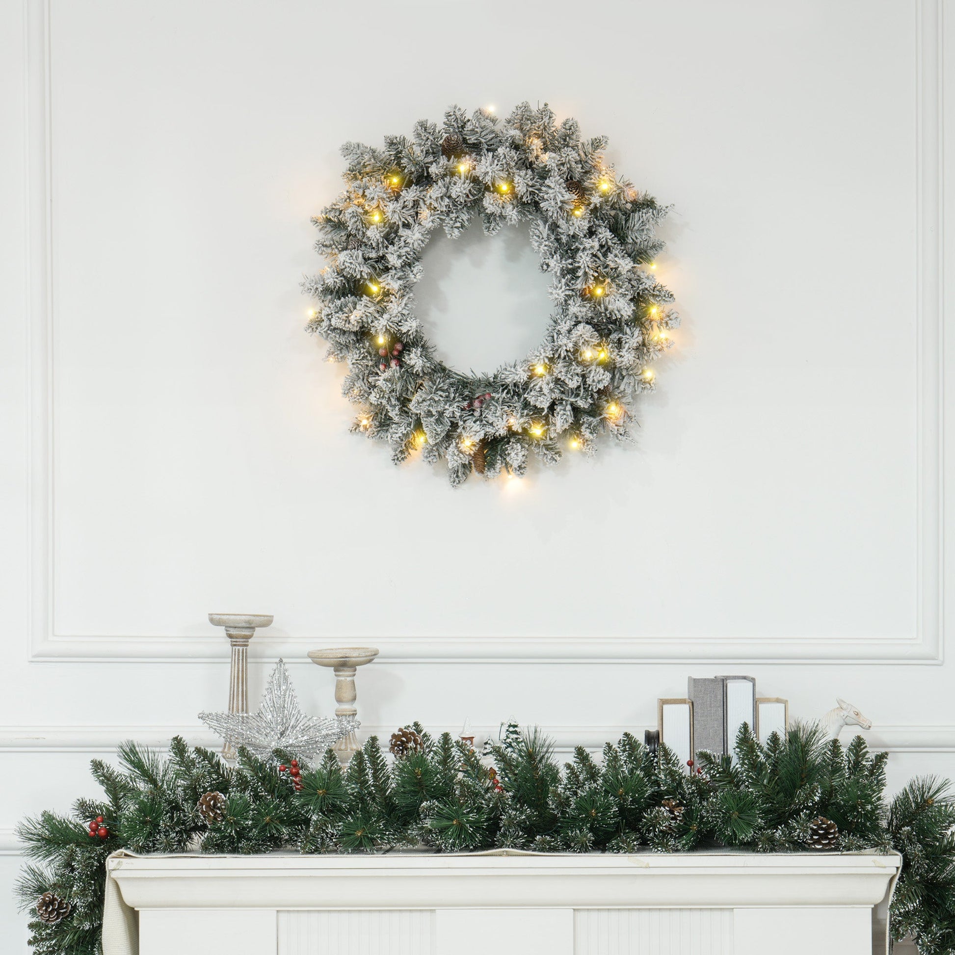 Snowy 60-inch Christmas wreath with pinecones, berries & warm LED lights styled above a festive mantle — lifelike branches in a cosy countryside setting.