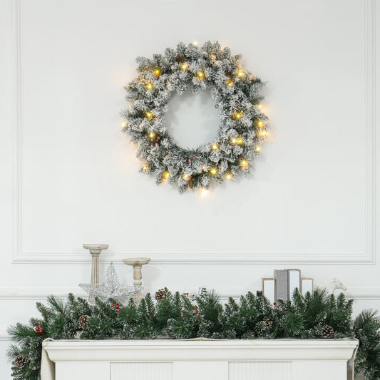 Snowy 60-inch Christmas wreath with pinecones, berries & warm LED lights styled above a festive mantle — lifelike branches in a cosy countryside setting.