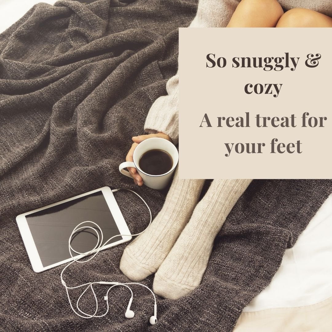 Soft cream cashmere sleep socks worn on feet, with coffee and tablet on a blanket in a cozy countryside-inspired setting.