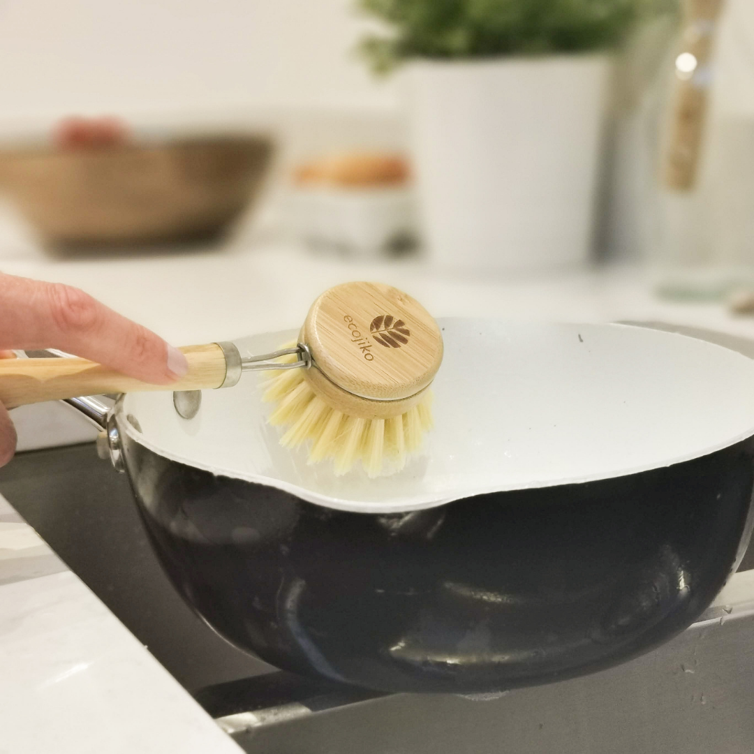 Wooden dish brush with bamboo handle in use on pan, part of eco kitchen cleaning set with rustic, natural styling