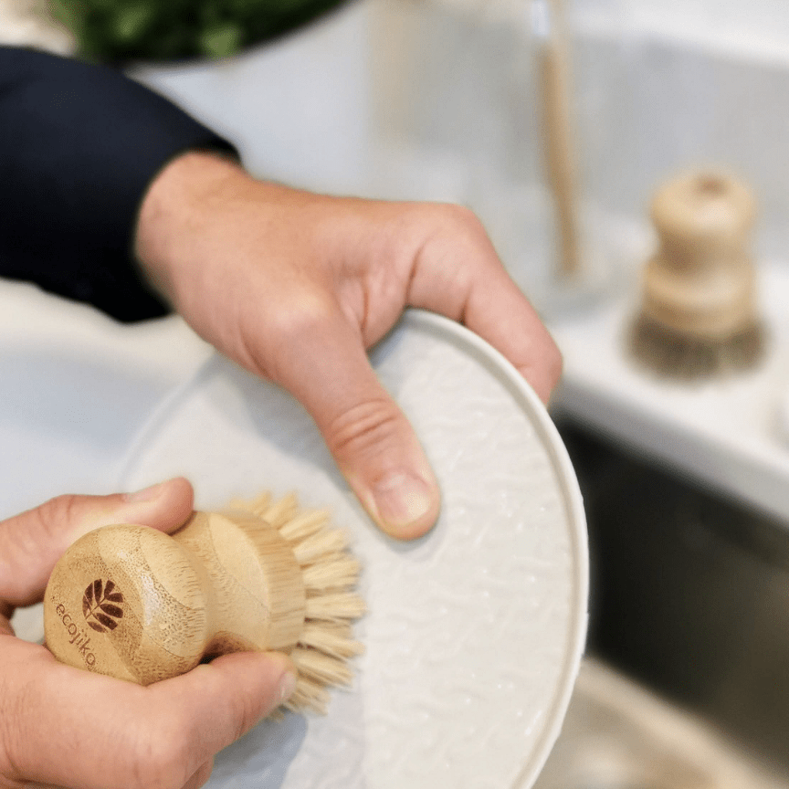Wooden dish brush with bamboo handle in use on ceramic plate, part of eco kitchen cleaning set with natural rustic styling