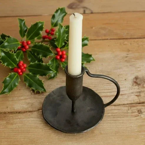 Rustic iron candle holder with white candle on wooden table beside holly leaves and red berries