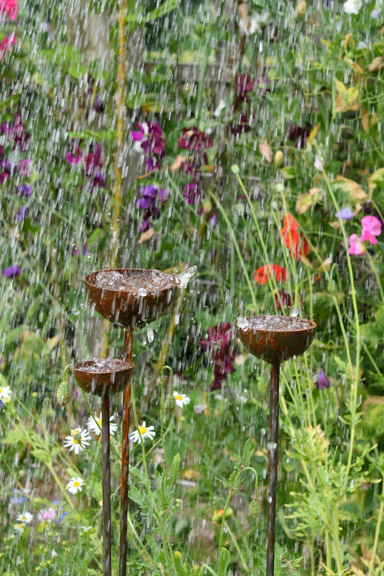 Rustic metal garden water fountains with falling water and colorful flowers in background