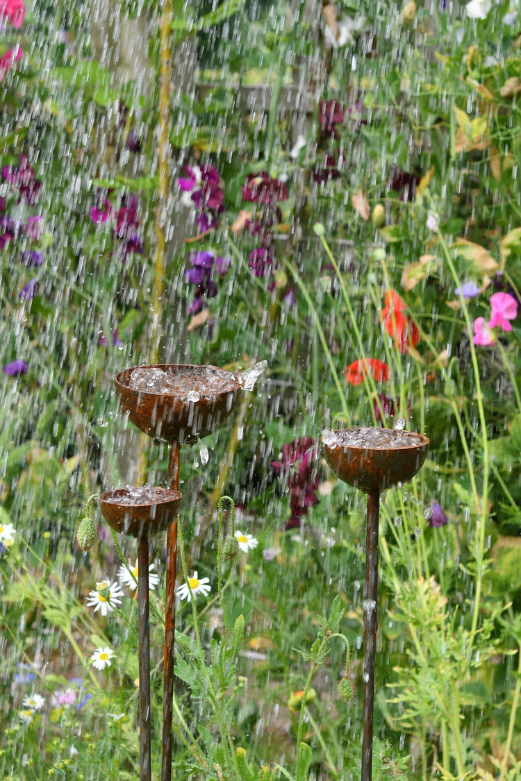 Rustic metal garden water fountains with falling water and colorful flowers in background