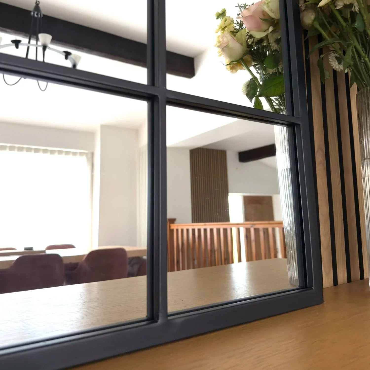heritage-inspired mirror with black grid frame reflecting modern interior with wooden beams and pink roses