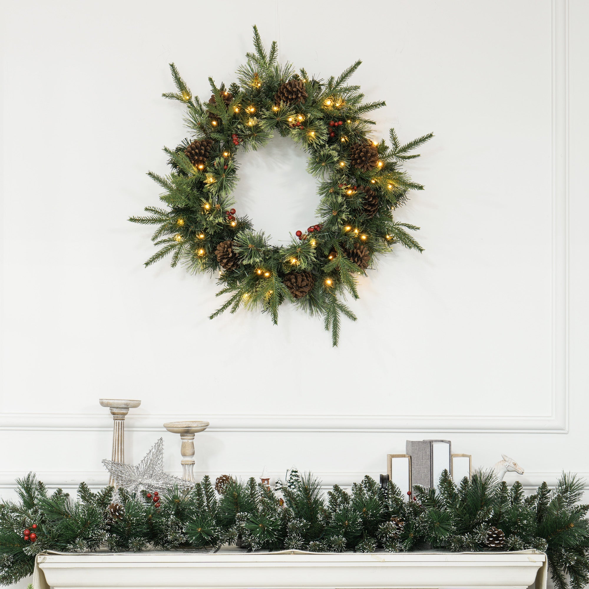 60-inch winter wreath with pinecones, berries & warm LED lights styled above a mantle — festive, lifelike branches in a rustic countryside setting.