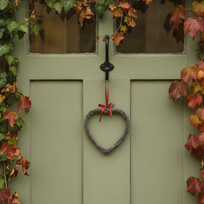 Heart-shaped wreath with a red ribbon hanging on a green door surrounded by autumn leaves.