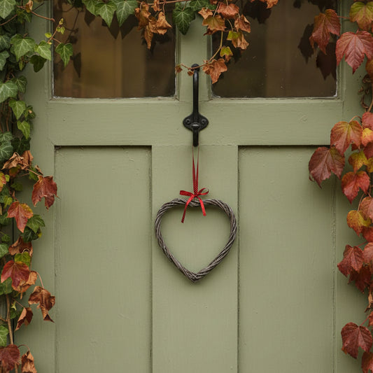 Heart-shaped wreath with a red ribbon hanging on a green door surrounded by autumn leaves.