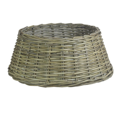 Large grey kubu rattan Christmas tree skirt styled beneath a decorated tree, surrounded by wrapped gifts. Rustic festive base with woven texture and tapered shape.