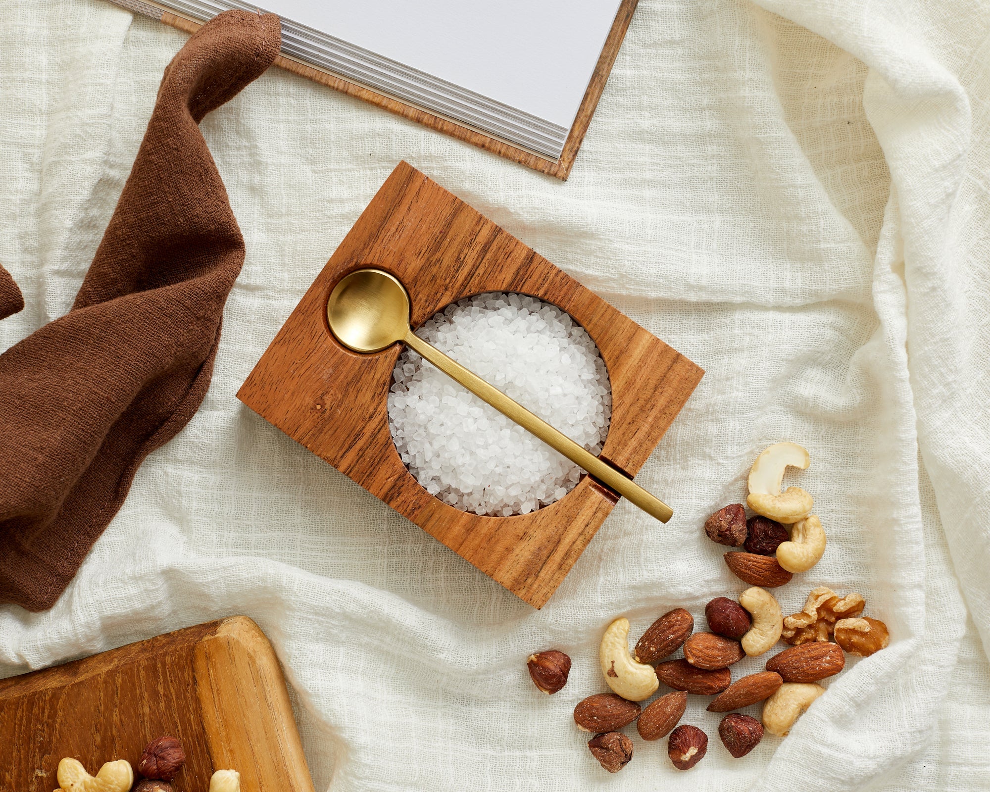 Acacia wood seasoning pot with brass spoon styled on linen with nuts and salt