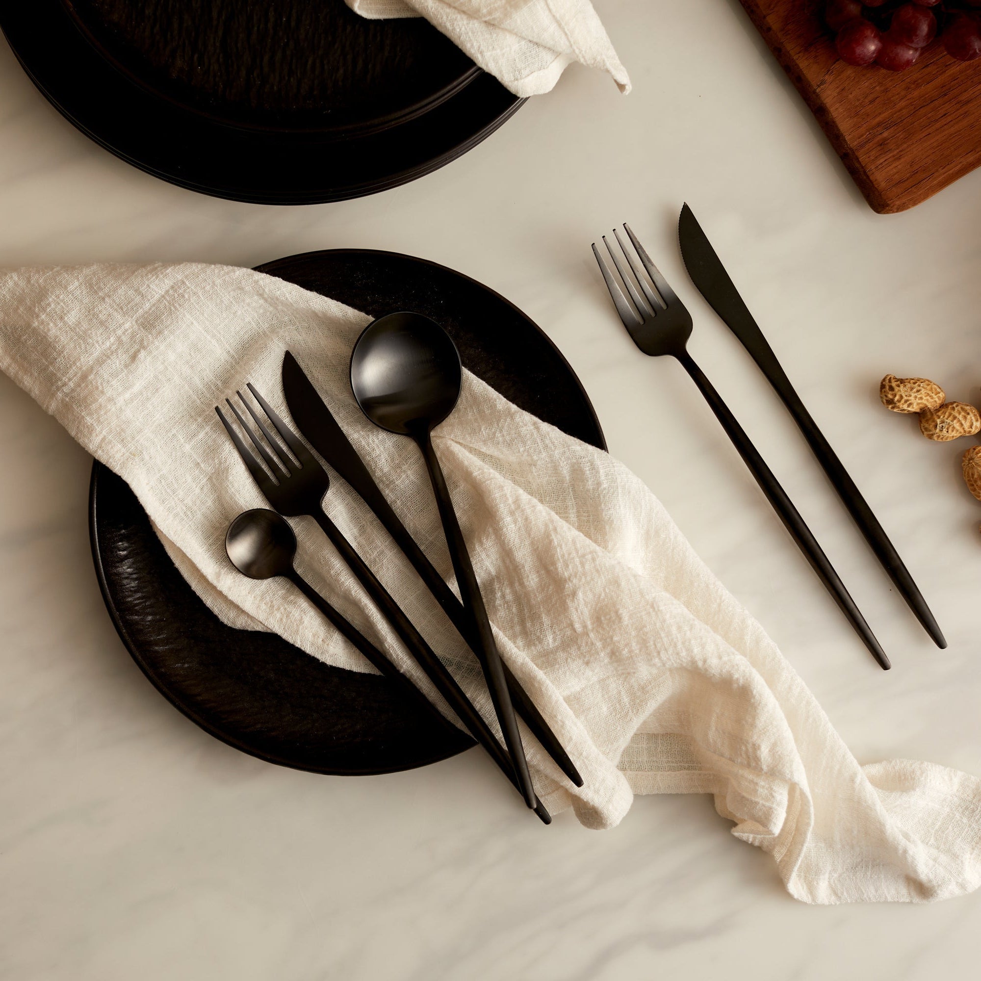 Alverley White cotton napkin styled on a black ceramic plate with black cutlery, all resting on a marble tabletop for refined countryside dining and poetic table layering.
