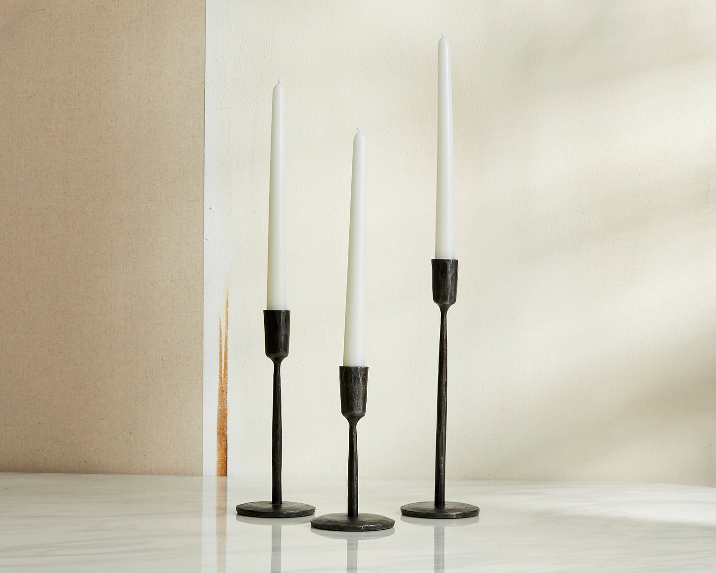 Keswick iron candle trio wrought black holders set on marble table with natural wall backdrop
