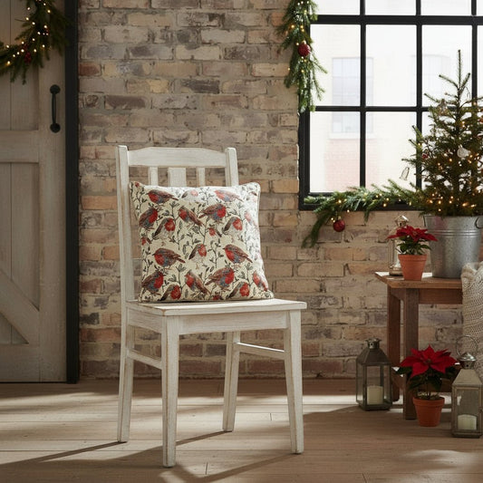 Robin tapestry cushion on whitewashed chair in festive room, warm woodland tones, rustic Christmas styling with countryside charm