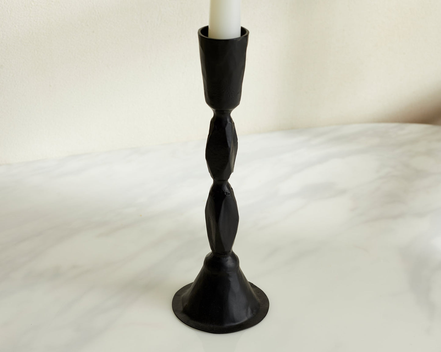 Closeup of sculptural black candle holder in blackened brass displayed on neutral background