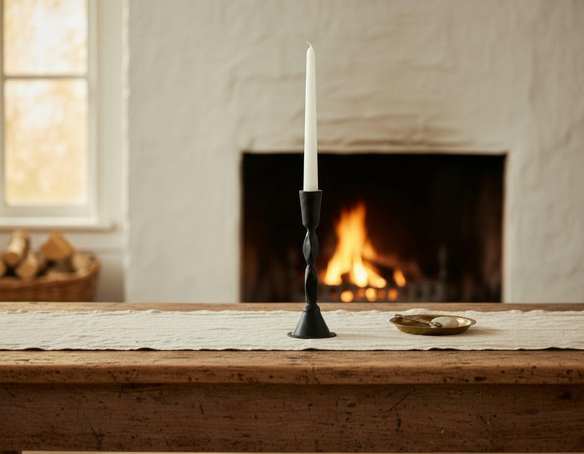 Sculptural black candle holder in blackened brass on coffee table in front of open fireplace
