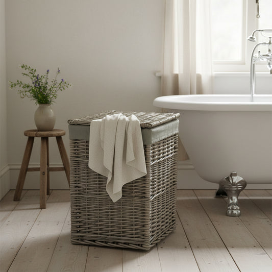 Square wicker laundry basket grey sage in bathroom with rolltop bath, milking stool and wooden floor
