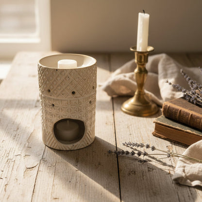 Stoneware wax melt burner with geometric pattern on wooden kitchen table with wax melt, candle holder, books, linen and lavender sprigs
