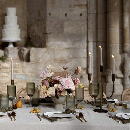 Elegant wedding reception with a long table set for dinner, floral centerpieces, and a cake against a stone wall.